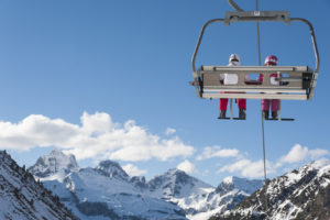 Chairlift full of skiers at a ski resort with snowy mountains on background